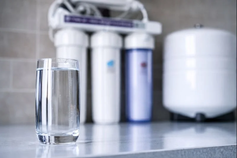 Verre d’eau posé devant un système de filtration de l’eau
